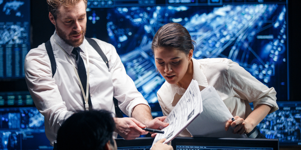 Analysts in a command center reviewing documents and intelligence data on large digital displays, collaborating to make real-time operational decisions.