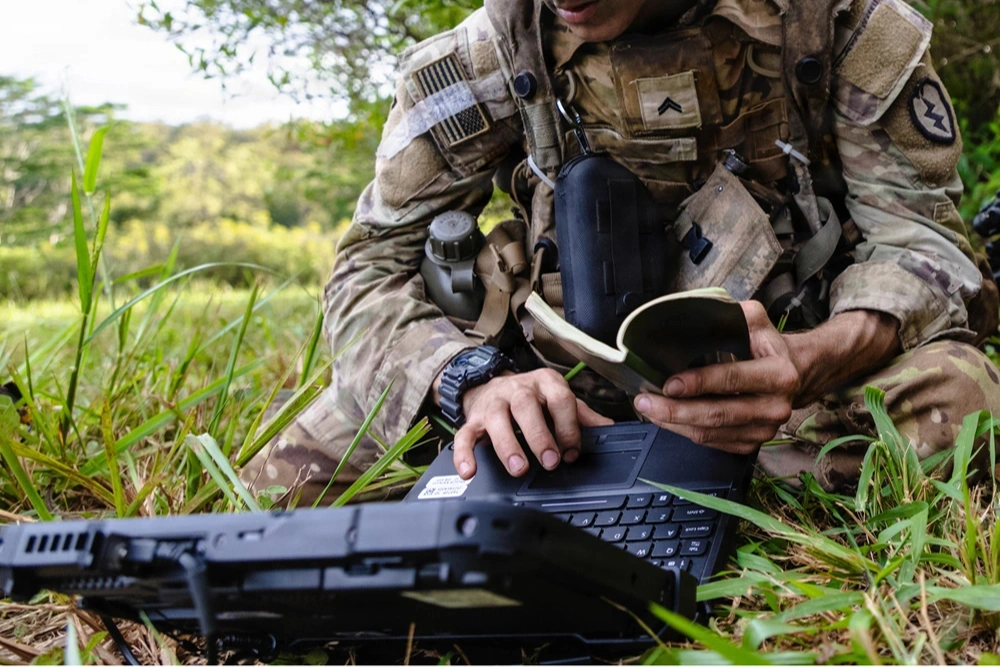 U.S. Military soldier in field consulting laptop
